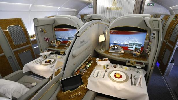 Innenansicht einer luxuriösen Emirates-Flugzeugkabine mit gedeckten Tischen und Bildschirmen.