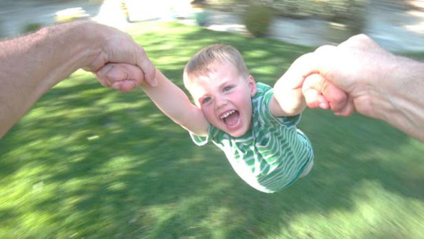 Ein lachender Junge wird von zwei Händen im Kreis geschwungen.