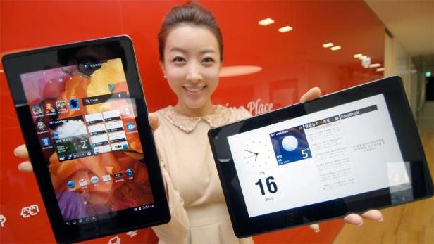 Eine Frau präsentiert zwei Tablets mit unterschiedlichen Apps vor einem roten Hintergrund.