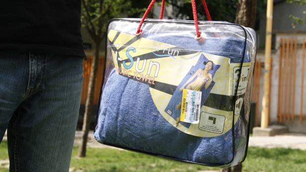 Eine Person trägt eine transparente Tasche mit einem blauen „Hi-Sun Music Towel“ Strandtuch.