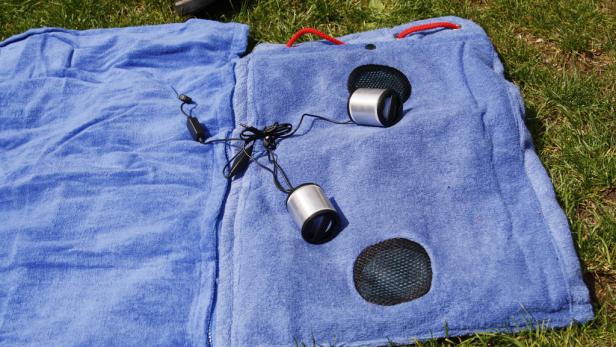Eine blaue Strandmatte mit integrierten Lautsprechern liegt auf einer Wiese.