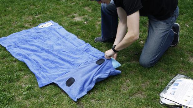Eine Person befestigt ein blaues, aufblasbares Kissen an einer blauen Strandmatte auf einer Wiese.