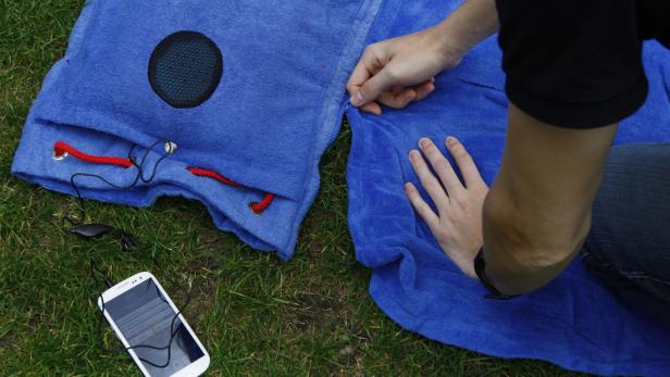 Eine Person schließt einen blauen Handtuch-Lautsprecher mit einem Reißverschluss.