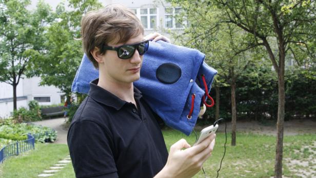 Ein Mann mit Sonnenbrille trägt eine blaue Lautsprechertasche über der Schulter und bedient sein Smartphone.