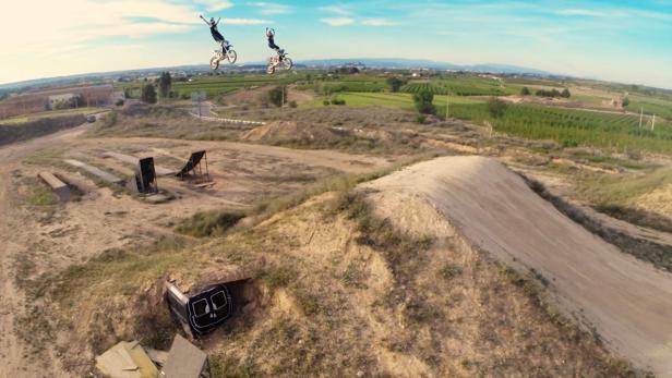 Zwei Motocrossfahrer springen mit ihren Motorrädern über eine Rampe.