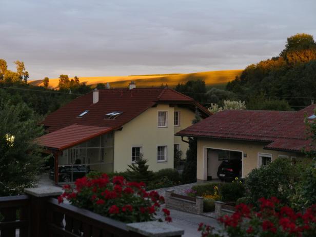 Ein Wohnhaus mit roten Ziegeln vor einer hügeligen Landschaft im Abendlicht.