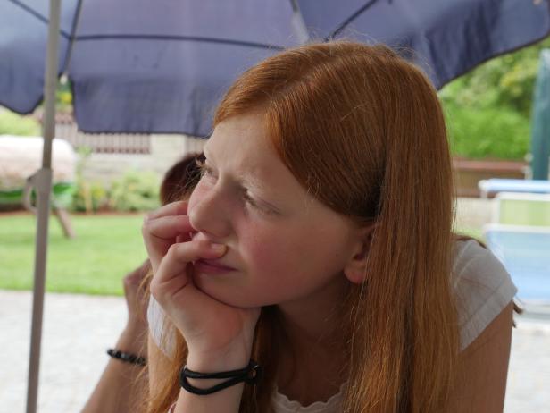 Ein rothaariges Mädchen sitzt nachdenklich unter einem Sonnenschirm.