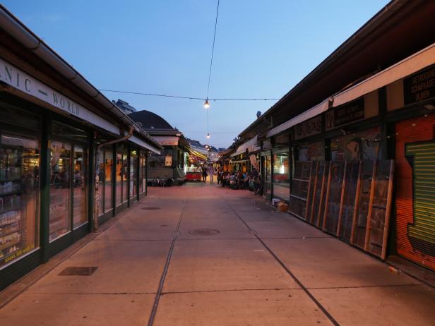 Blick durch einen belebten Marktgang mit Imbissständen und Geschäften am Abend.