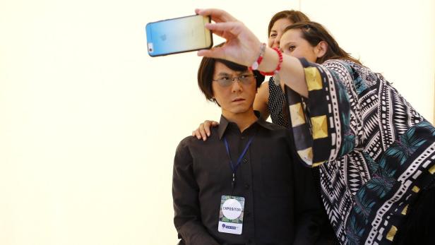 A visitor takes a selfie beside a Geminoid HI-2 ro