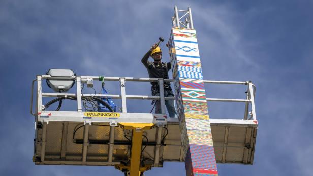 Ein Bauarbeiter auf einer Hebebühne montiert einen hohen Turm aus bunten Legosteinen.