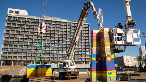 Ein Kran hebt bunte, dekorierte Blöcke in die Höhe, um ein Bauwerk zu errichten.