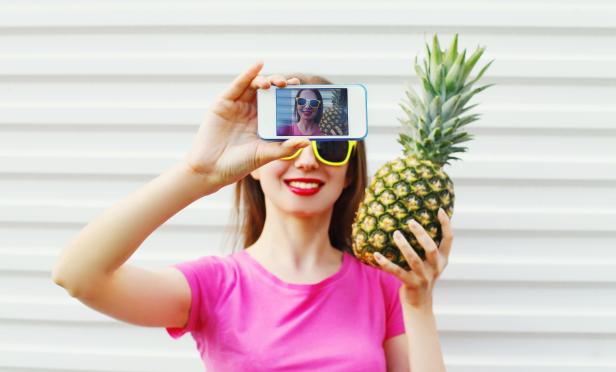 Fashion girl with pineapple taking picture self portrait on smartphone