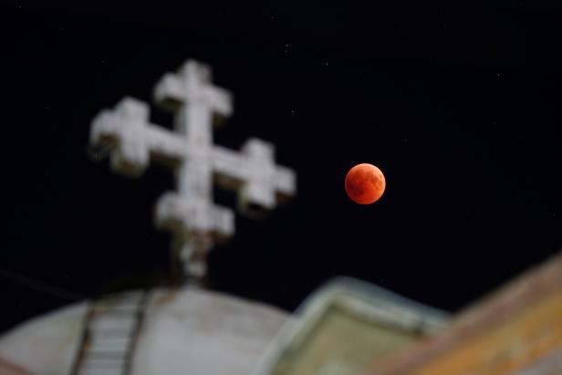 The moon is seen during a lunar eclipse over the Coptic Orthodox Patriarchate Church in Amman