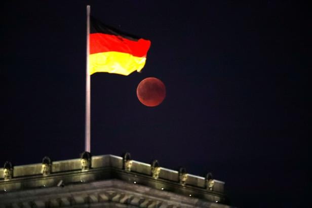 The moon is seen during a lunar eclipse next to the German national flag on top of the Reichstag building in Berlin