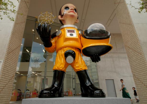 People walk by a statue of a child wearing what appears to be a hazardous material suit in Fukushima