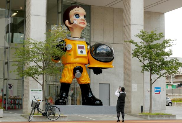 A woman takes a picture of a statue of a child wearing what appears to be a hazardous material suit in Fukushima