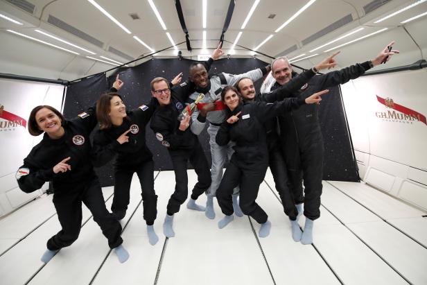 Retired sprinter Usain Bolt poses with staff members holding a bottle of "Mumm Grand Cordon Stellar" champagne after they enjoy zero gravity conditions during a flight in a specially modified Airbus Zero-G plane above Reims