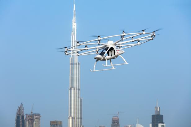 Ein Volocopter-Flugtaxi fliegt vor der Skyline von Dubai mit dem Burj Khalifa im Hintergrund.