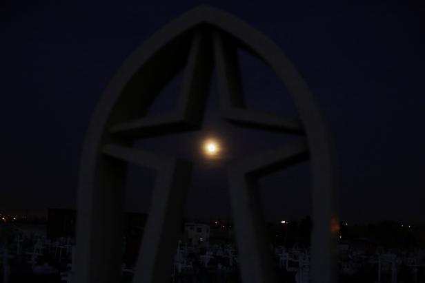 The full moon is seen through a headstone ahead of a total lunar eclipse, known as the "super blood wolf moon", at a cemetery in Ciudad Juarez