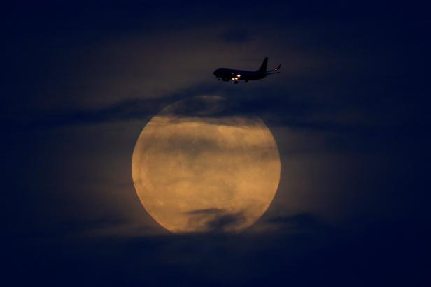 A  plane passes  as the moon rises through clouds before start of total lunar eclipse in California