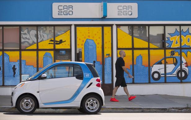 A man walks past an electric car from the car sharing company Car2Go, shown parked in front of their offices in San Diego