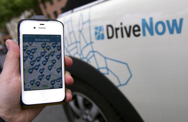 FILE PHOTO: Picture illustration shows a smartphone displaying the DriveNow app with available cars in Berlin's city centre held up next to a car from the DriveNow service in Berlin