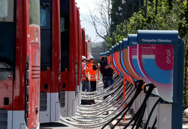 Men supervise the electric chargers for the new fleet of electric buses for public transport manufactured by China's BYD, in a bus terminal in Santiago