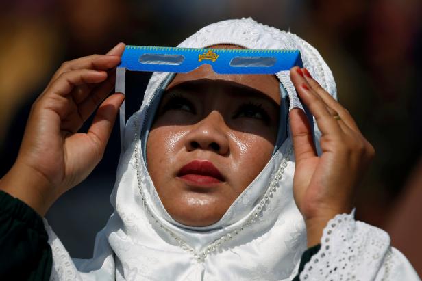 A muslim woman wearing hijab observes the annular solar eclipse before taking part in a mass prayer in Siak