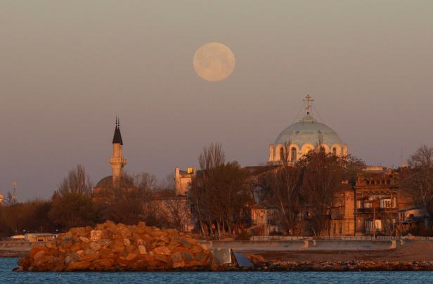 The supermoon sets behind a mosque and an Orthodox cathedral during sunrise in Yevpatoriya