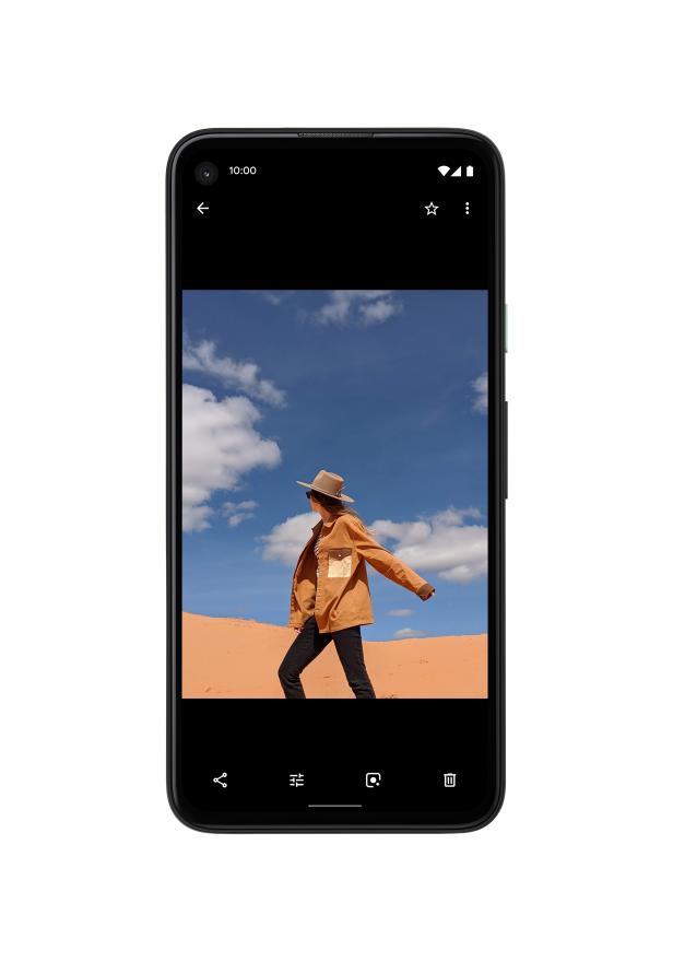 Eine Frau mit Hut und Jacke steht in einer Wüste unter blauem Himmel.