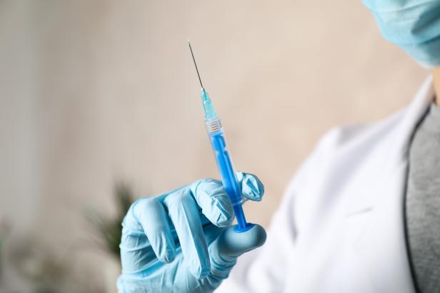 Doctor holds medical syringe of vaccine, injection on brown background. Coronavirus protection. Healthcare and medical concept