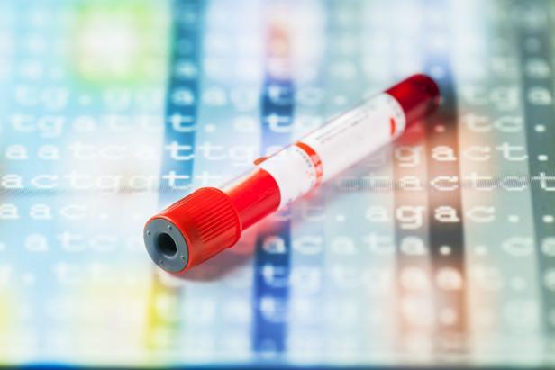Ein rotes Blutentnahmeröhrchen liegt vor einem Hintergrund mit DNA-Sequenzen.