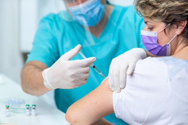 Female patient with face mask looking at her arm while getting flu shot