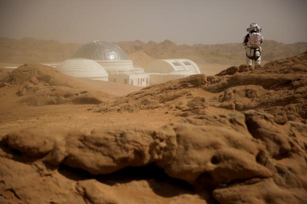 Sand whipped up by wind shrouds the C-Space Project Mars simulation base as a staff member wearing a mock space suit poses in the Gobi Desert outside Jinchang