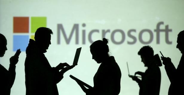 FILE PHOTO: Silhouettes of laptop and mobile device users are seen next to a screen projection of Microsoft logo in this picture illustration