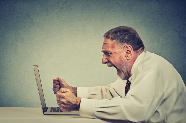 Angry senior business man working on computer screaming