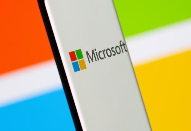 Smartphone is seen in front of Microsoft logo displayed in this illustration taken