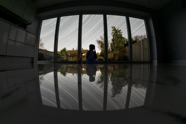 Kind vor Fenster und Spuren von Sternen am sich bewegenden Nachthimmel