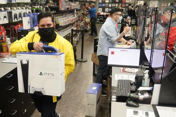 Inside a GameStop store a worker takes a Sony PS5 gaming console to the counter to sell