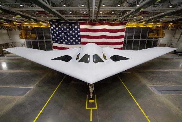 Ein B-21 Raider Tarnkappenbomber steht vor einer großen US-Flagge.