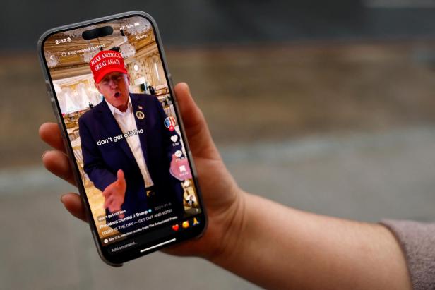 A woman poses with her smartphone displaying the @realdonaldtrump TikTok page, in Washington