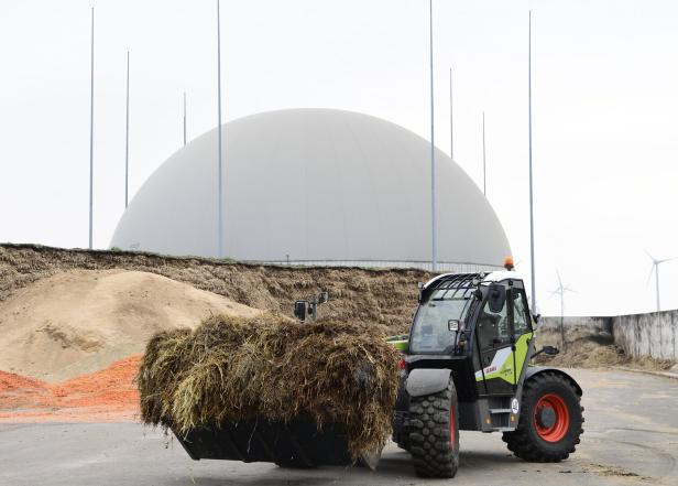 Ein Claas Scorpion Teleskoplader mit einer vollen Schaufel vor einer Biogasanlage.