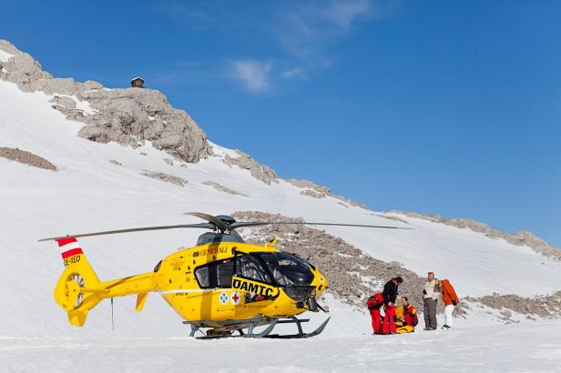 Ein gelber ÖAMTC-Rettungshubschrauber steht im Schnee, während Sanitäter sich um eine Person kümmern.