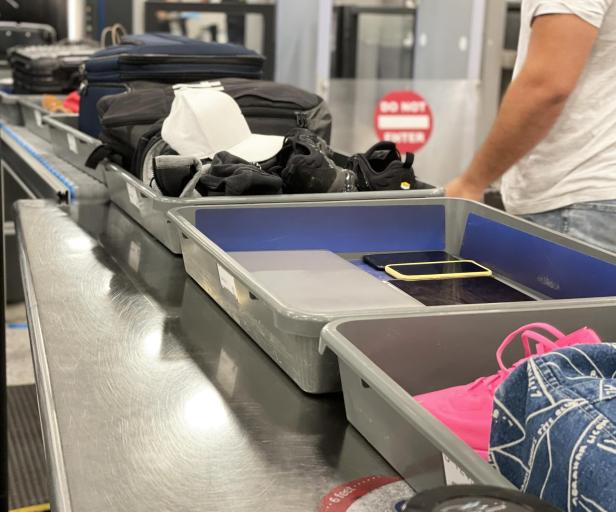 Es kann passieren, dass US-Grenzbeamte elektronische Geräte aus dem Handgepäck konfiszieren (Symbolbild). Graue Plastikboxen gefüllt mit Handgepäck, darunter elektronische Geräte, in einer Flughafen-Sicherheitskontrolle.