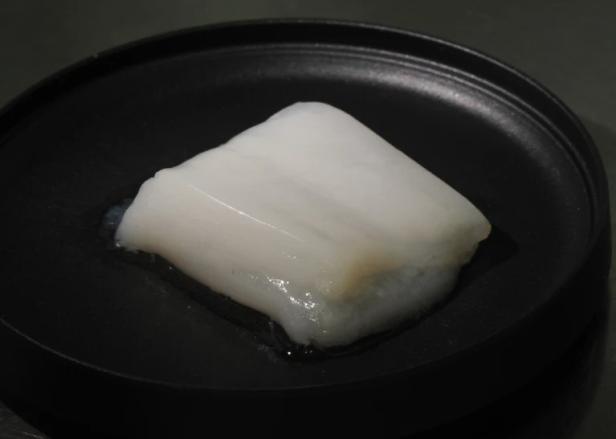 Das Stück Fleisch aus dem Labor der Universität von Tokio ist 7 × 4 Zentimeter groß. ein beinahe weißes Stück Hendlfleisch auf einem schwarzen Teller