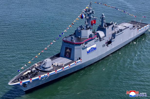 Ein großes graues Kriegsschiff mit nordkoreanischer Flagge fährt geschmückt mit bunten Wimpeln auf dem Wasser.