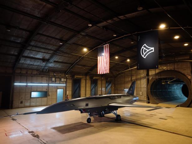 Ein YFQ-44A-Flugzeug steht in einem Hangar mit einer US-Flagge und einem Banner.