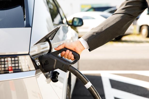 An den E-Ladestationen von Wien Energie kann Tag und Nacht das Elektroauto aufgeladen werden. Ein Mann im Anzug lädt sein E-Auto an einer Ladestation von Wien Energie auf.