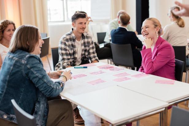 Menschen sitzen an einem Tisch mit Notizen und scheinen sich angeregt zu unterhalten.