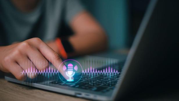 Eine Person nutzt einen Laptop, auf dem ein Mikrofon-Symbol angezeigt wird.